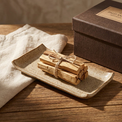 Palo santo sticks tied with twine on a ceramic plate with a branded box in the background.