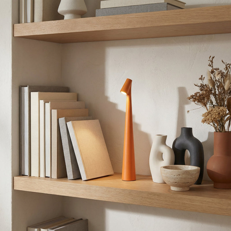 Shelving unit with books, a tall orange lamp, and decorative items against a neutral wall.