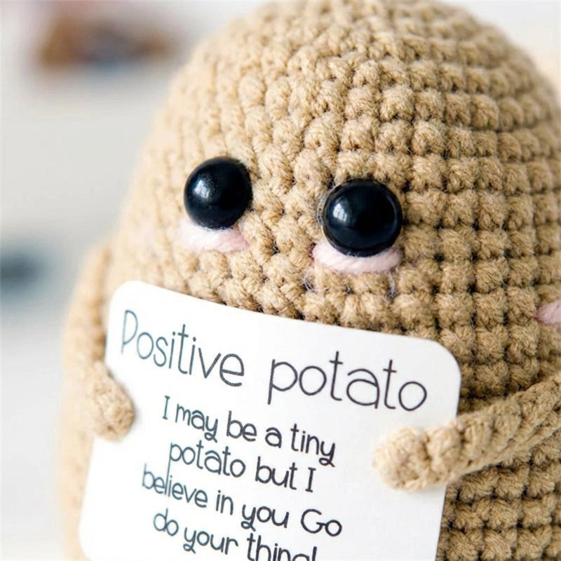 Crocheted potato plush toy with a sign saying 'Positive potato' on a blurred background