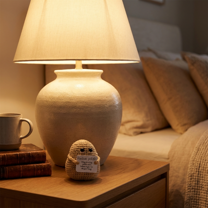 Lamp on a bedside table with a small plush toy and books, next to a bed.
