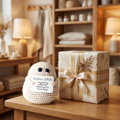 Decorative knitted potato with a message and a gift box on a wooden surface.