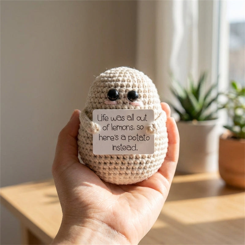 Hand holding a crocheted potato with a humorous message in a home setting