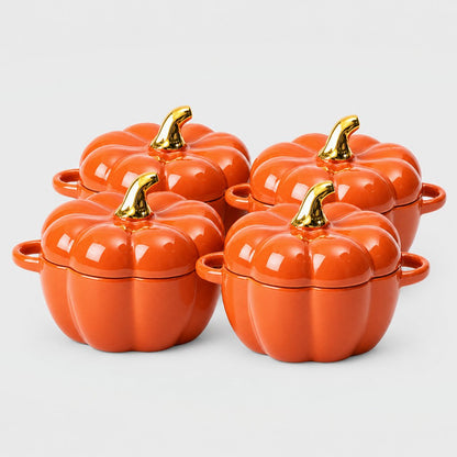 Set of four glossy orange ceramic pumpkin bowls with gold stems and loop handles arranged in two rows on a plain light backdrop