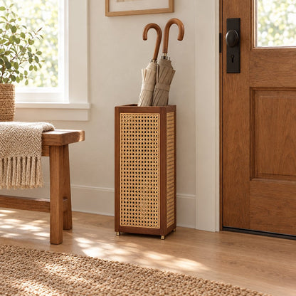 Rattan cane umbrella stand with a dark wood frame holding two wooden handled umbrellas beside a wooden bench with a knit throw and a brown front door