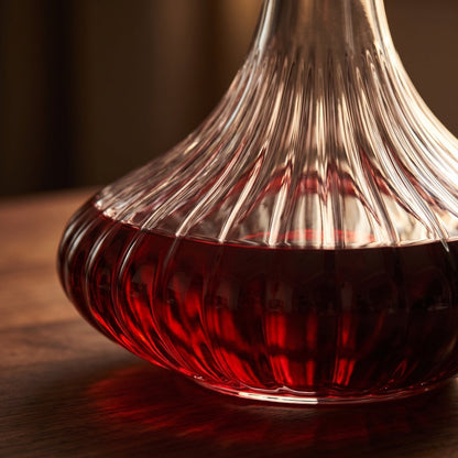Close-up of the ribbed glass base of a wine decanter filled with red wine on a dark wood surface