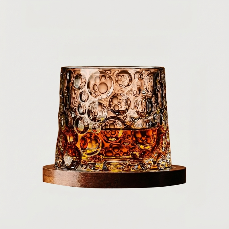 Textured rotating whiskey glass with amber whiskey on wood coaster