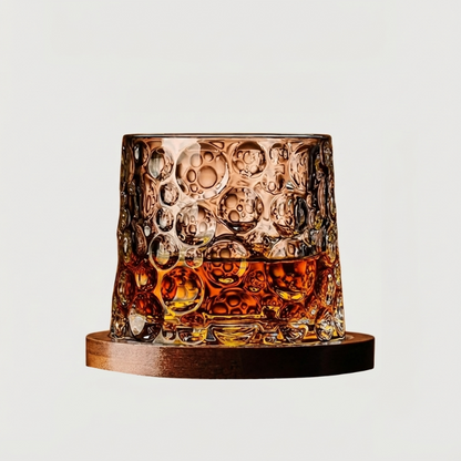 Textured rotating whiskey glass with amber whiskey on wood coaster