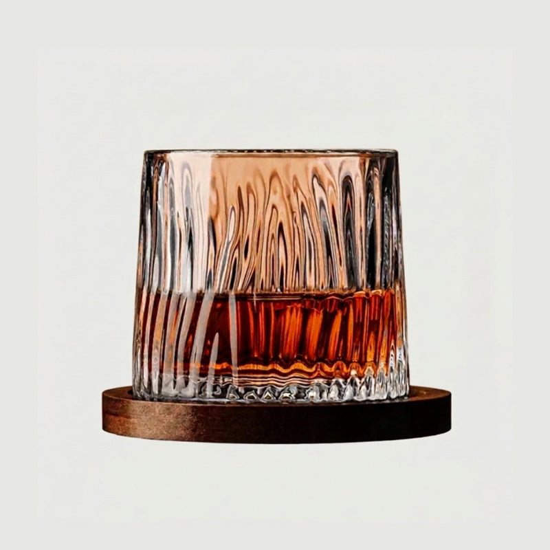 Textured rotating whiskey glass with amber whiskey on wood coaster with white background.