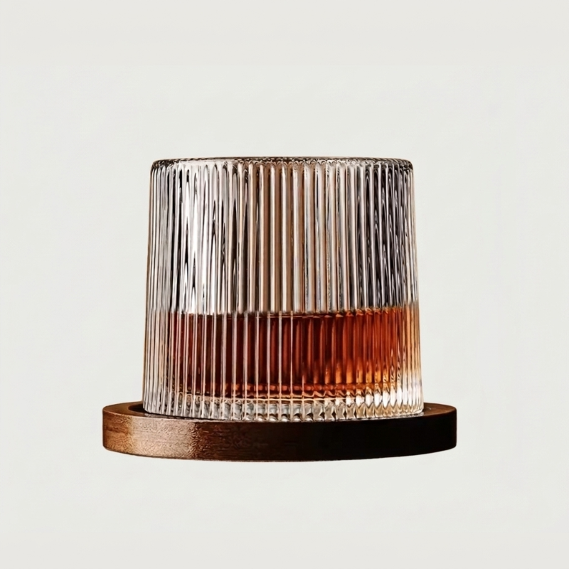 Ribbed rotating whiskey glass with wood coaster on white background