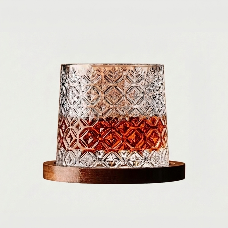 Faceted rotating whiskey glass with amber base on wood coaster