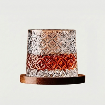 Faceted rotating whiskey glass with amber base on wood coaster
