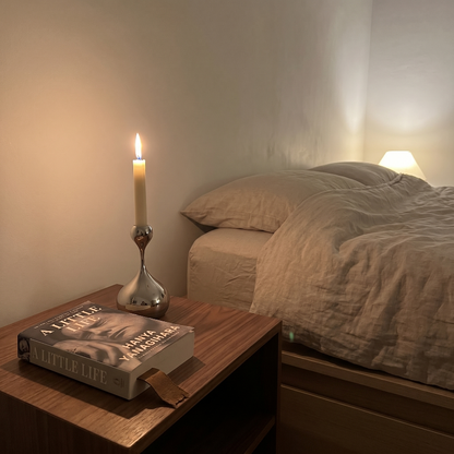 Sculpted chrome taper candle holder on bedside table in softly lit bedroom