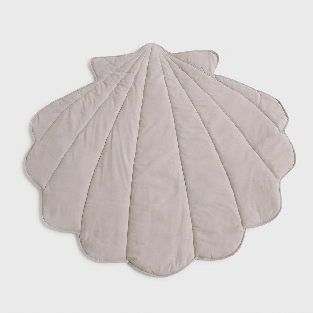 A scalloped shell-shaped quilted blanket in a light taupe-beige color, displayed flat against a neutral light gray background.