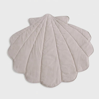 A scalloped shell-shaped quilted blanket in a light taupe-beige color, displayed flat against a neutral light gray background.