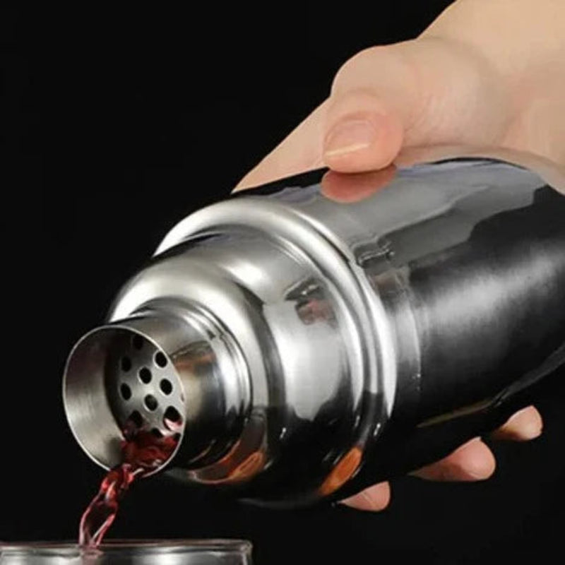 Silver stainless steel cocktail shaker pouring a cocktail into a glass.