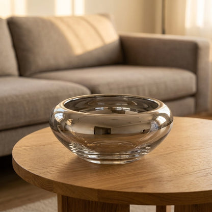 Empty mirrored silver glass bowl on a round wooden coffee table in a living room with a beige sofa