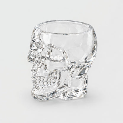 Single empty large clear glass skull glass with a faceted open bowl, molded skull face and thick faceted base, on a plain light gray background