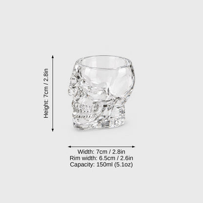 Medium clear glass skull glass on a light gray background with dimension labels: height 7 cm or 2.8 in, width 7 cm or 2.8 in, rim width 6.5 cm or 2.6 in, capacity 150 ml or 5.1 oz