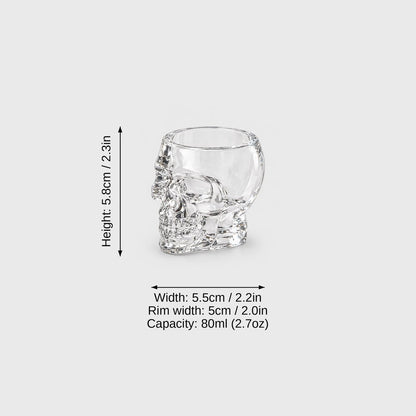 Small clear glass skull glass on a light gray background with dimension labels: height 5.8 cm or 2.3 in, width 5.5 cm or 2.2 in, rim width 5 cm or 2.0 in, capacity 80 ml or 2.7 oz