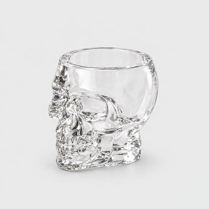 Single empty clear glass skull glass with a faceted skull face and open bowl on a thick clear base, on a plain light gray background