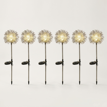 Six dandelion-shaped solar garden lights in a row, each with a glowing wire head, small solar panel and pointed ground stake, on a plain light background