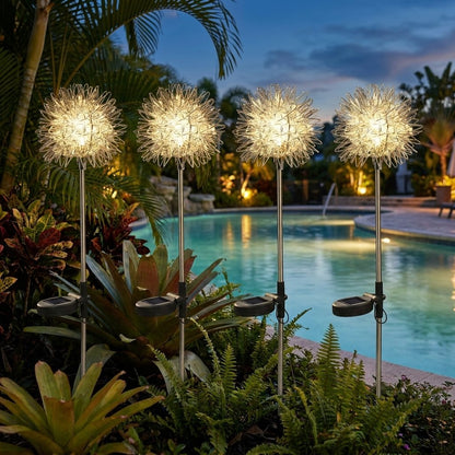 Four dandelion-shaped solar lights glowing among tropical plants beside a lit swimming pool at dusk