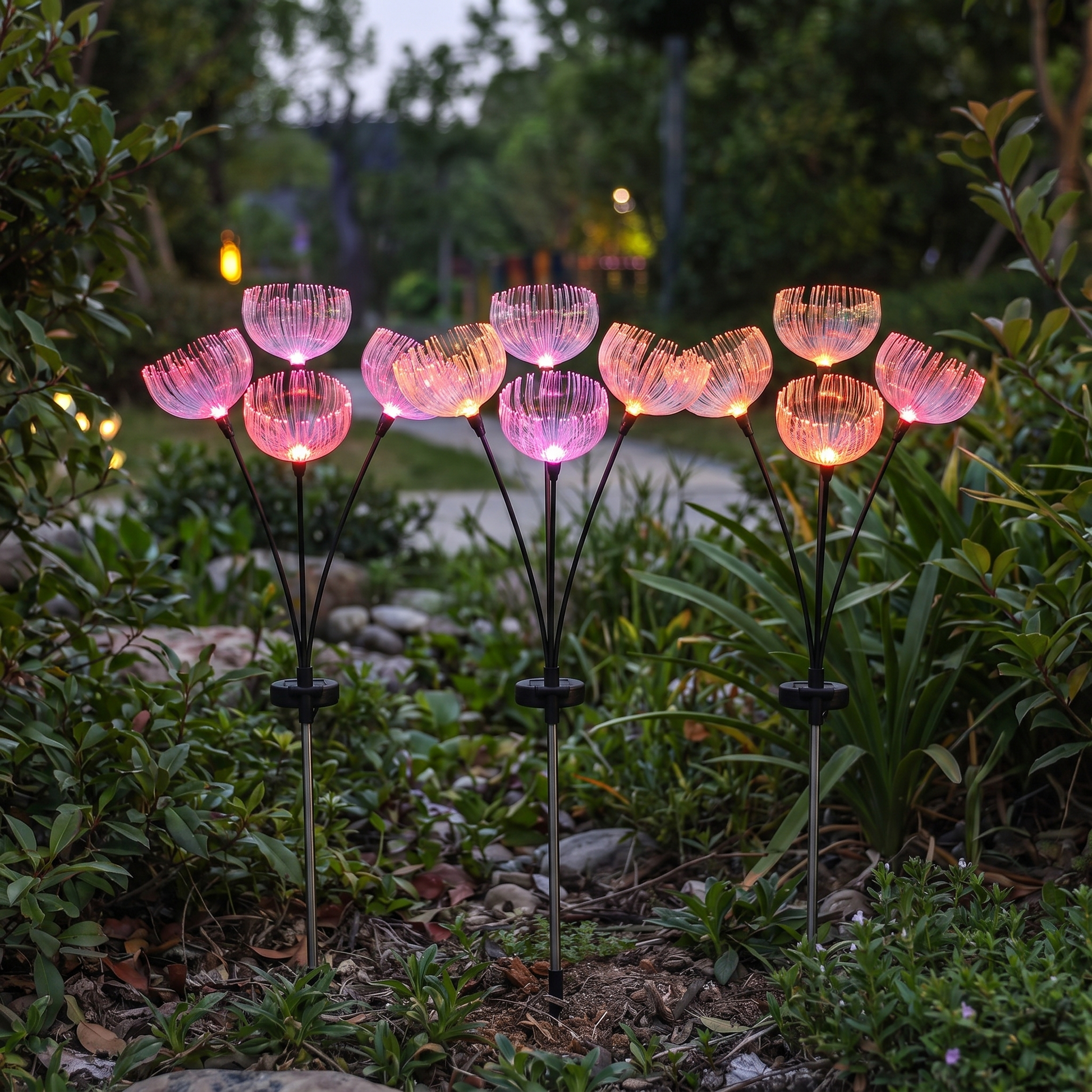Three color-changing jellyfish-style fiber-optic solar garden light stakes glowing in a garden bed