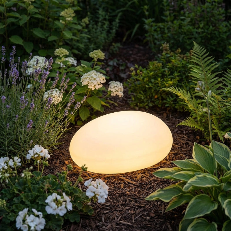 Round garden light surrounded by plants and flowers in a garden setting