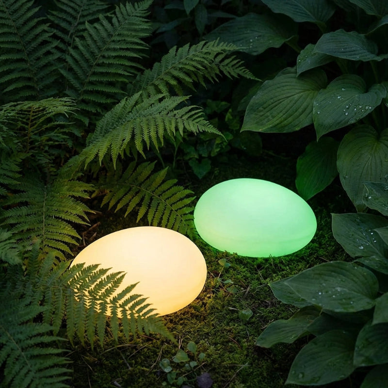 Two solar light stones, one yellow and one green, on a grassy ground with leaves in the background.