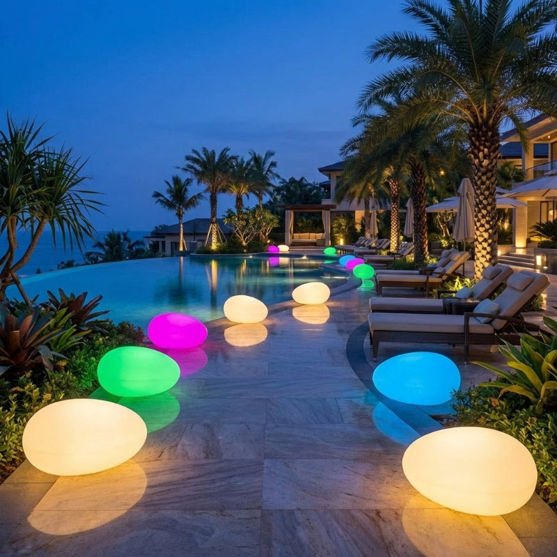 Colorful illuminated floating lights in a pool surrounded by palm trees and lounge chairs.