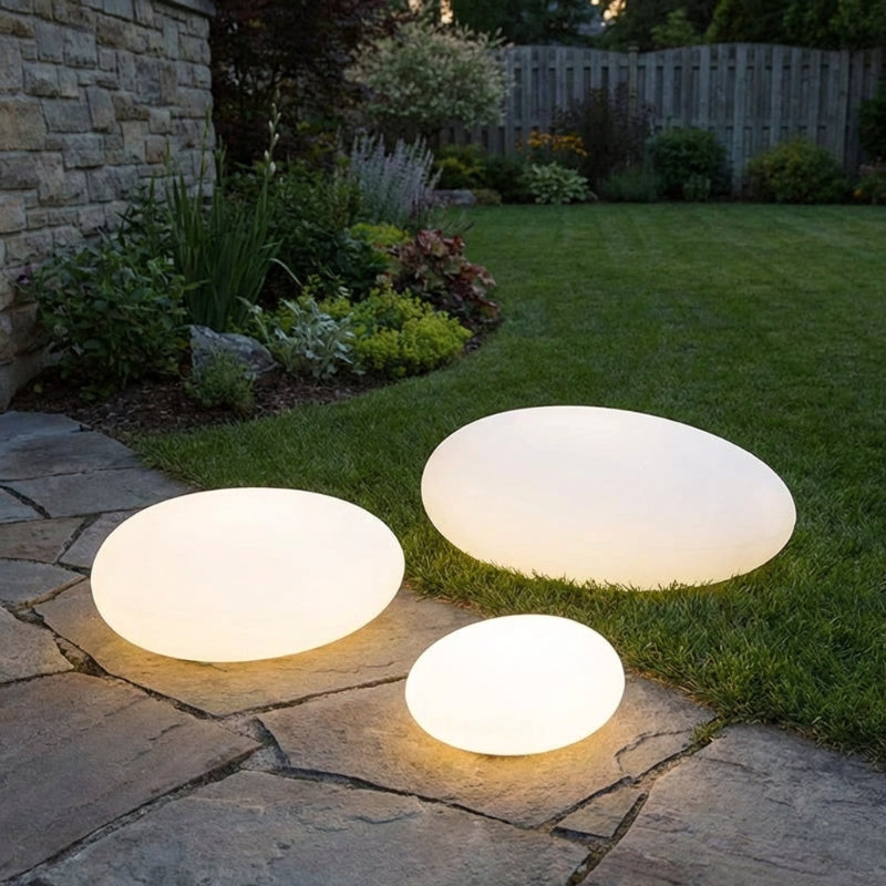 Three illuminated garden lights on a stone pathway with grass and plants in the background.