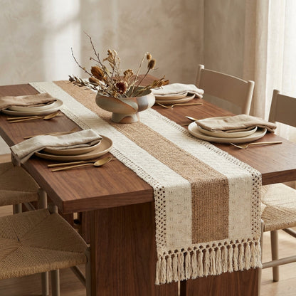 Dining table set with a striped table runner, plates, and chairs in a room with neutral decor.