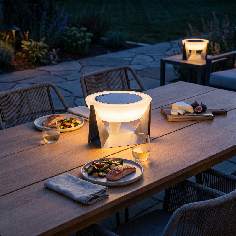 Stainless steel solar lamp on outdoor table with drinks at dusk