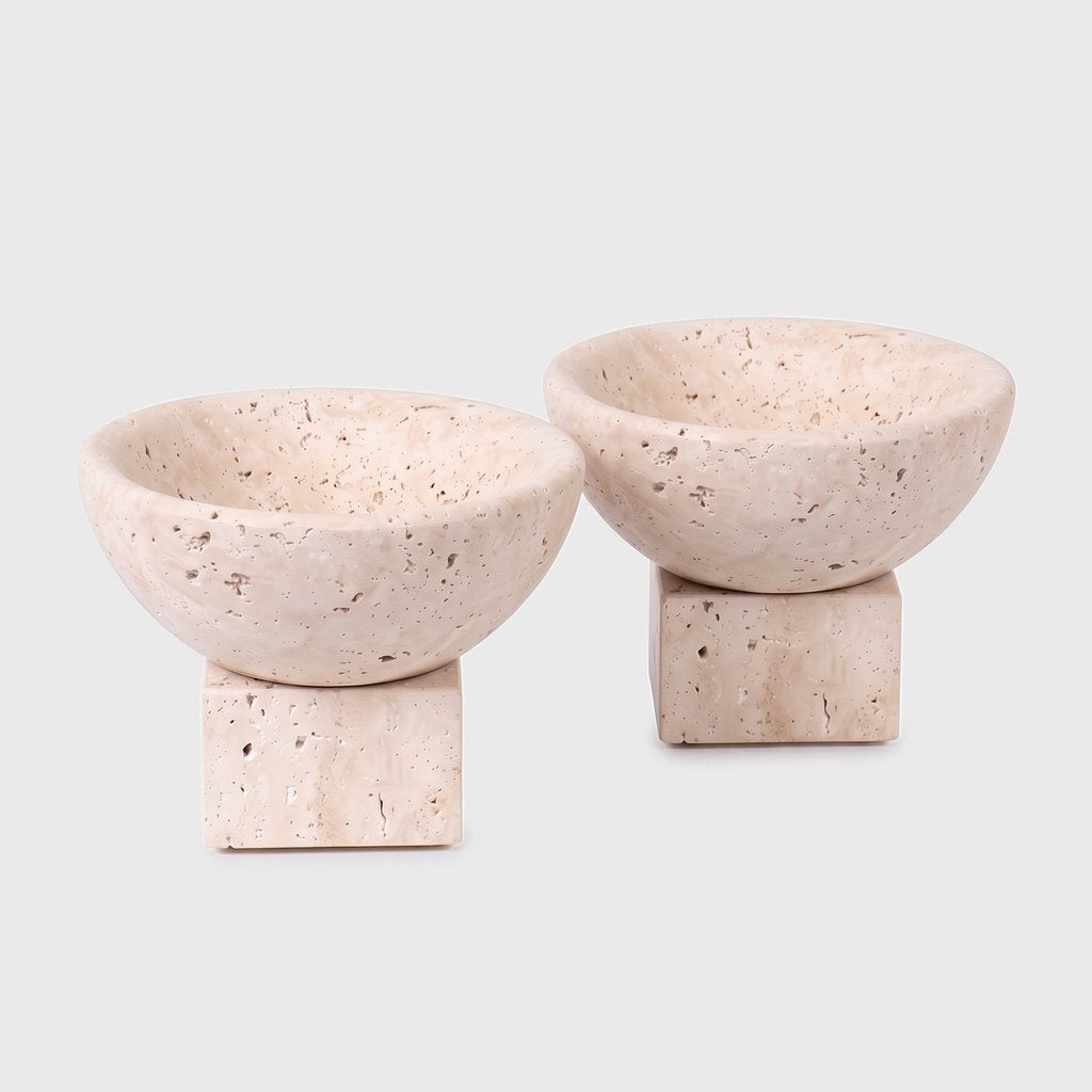 Two pale stone pedestal bowls with square bases on a plain light background