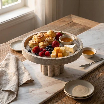 Travertine platter with pastries, fruits, and cheese on a wooden table.