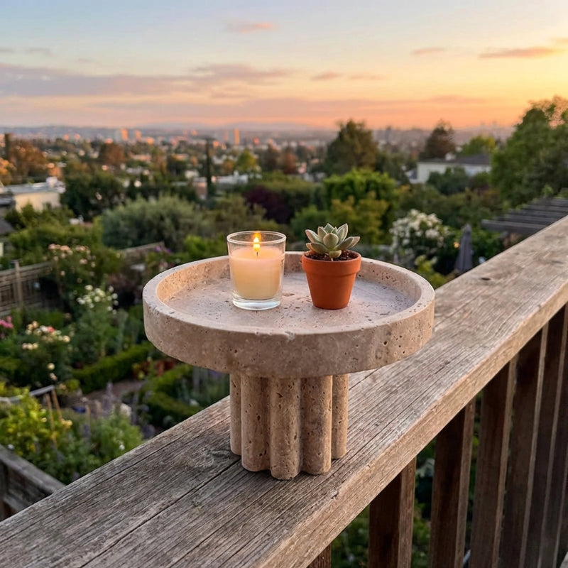Travertine tray with a candle and small plant on a railing overlooking a cityscape at sunset.
