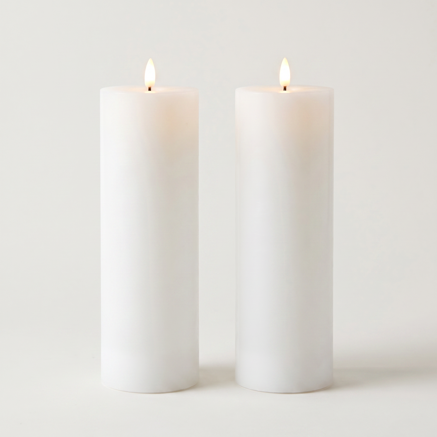 Set of two tall white waterproof LED flameless pillar candles on an off-white background