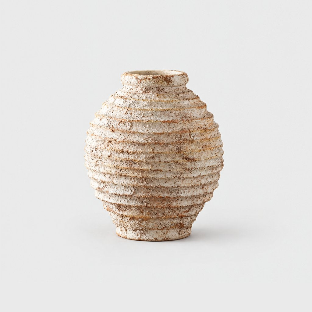 Small rounded textured cream and tan vase with horizontal ridges and a narrow rim, on a plain light gray background