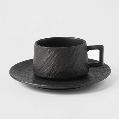 Black textured ceramic cup on a matching saucer on a plain light background