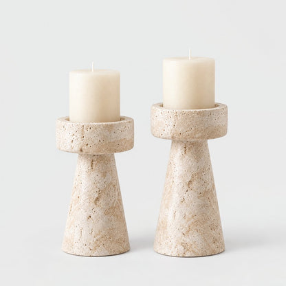 Set of two cream travertine pillar candleholders in medium and large sizes with cream pillar candles on a light grey background