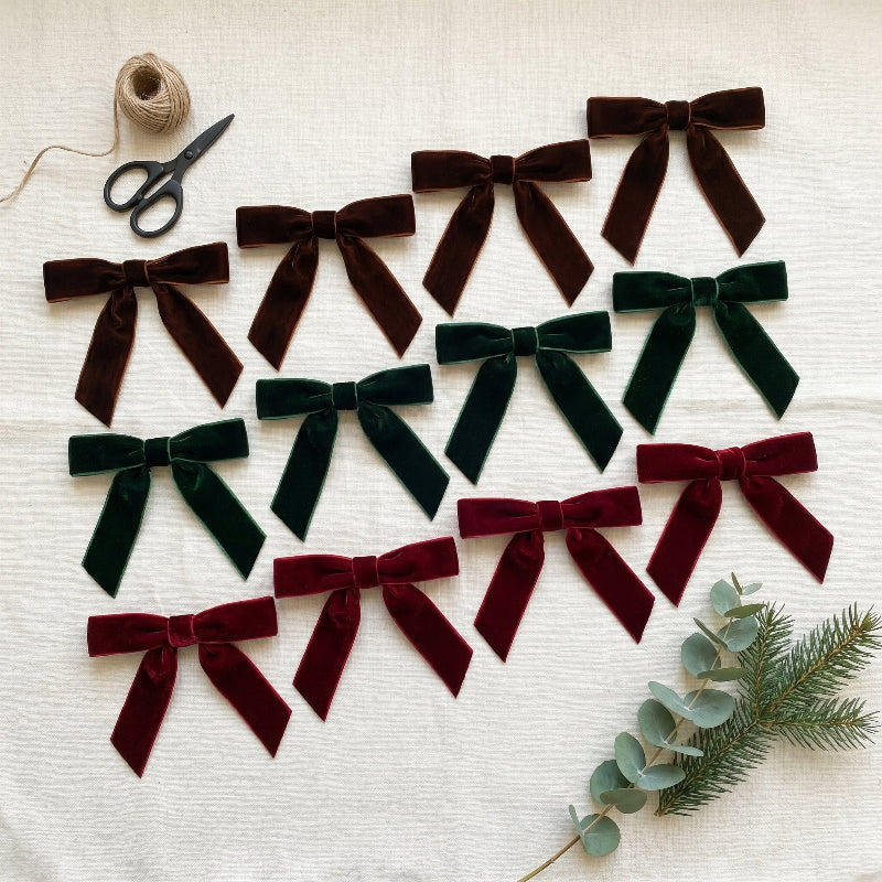12 velvet bows in burgundy, green, and brown on neutral linen surface