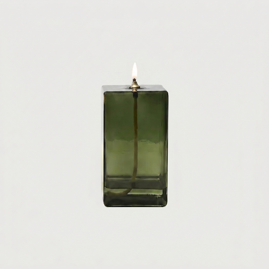 Green glass candle holder with a lit candle on a white background