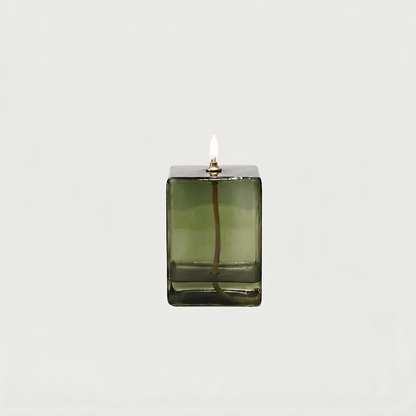 Green glass candle holder with a lit candle on a white background
