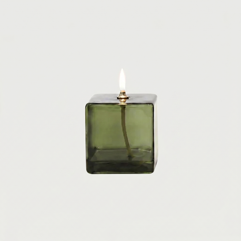 Green glass candle holder with a lit candle on a white background