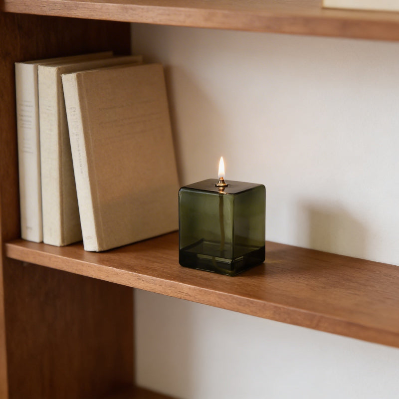 Green candle in a glass holder on a wooden shelf with books