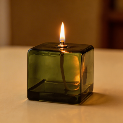 Green glass candle holder with a lit candle on a neutral background