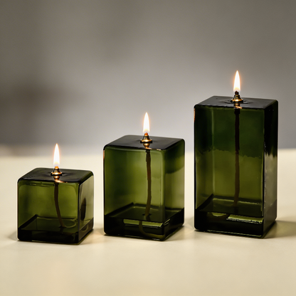 Three green square glass candles with lit wicks on a neutral background
