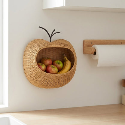 Apple-shaped rattan wall basket mounted in a kitchen next to a paper towel holder, holding apples and a banana