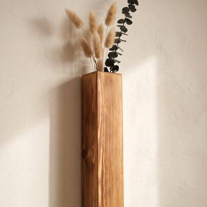 Close-up of a narrow brown wood wall planter holding pampas grass and a dark eucalyptus stem against a cream wall