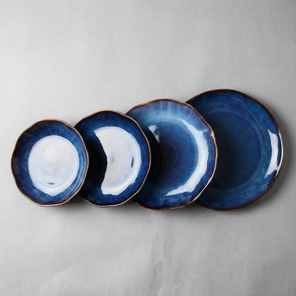 Set of four blue ceramic plates with gold rims on a gray background
